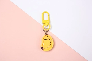 Macro detail of cute yellow resin banana keychain with a smiling face and spring hook