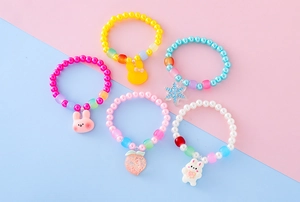 Dettaglio di cinque braccialetti di perline colorate con pendenti animali e ciondolo pesca
