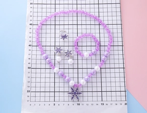 Close-up of children's purple snowflake beaded necklace, bracelet, and ring jewelry set