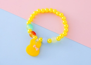 Dettaglio di un braccialetto di perle gialle per bambini con un simpatico coniglio
