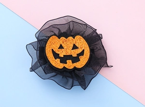 Detail of Halloween pumpkin hair clip with orange glitter and black mesh veil on a pink background