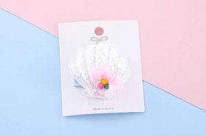 Detail of shell hair clip with white sequins and a pink bow on a display card