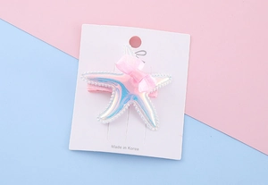 Close-up of pink laser starfish hair clip with bow on display card
