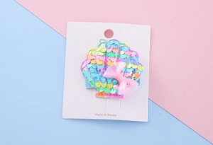 Close-up of shell hair clip with rainbow sequins and pink mesh bow on a card