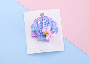 Detail view of purple sequin shell hair clip with pink mesh bow on display card