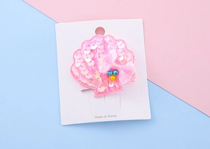 Detailed view of a pink sequin shell hair clip with a chiffon bow on a display card