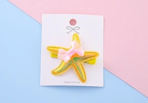 Detail of a yellow starfish hair clip with pink mesh bow on a display card for girls
