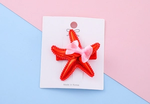 Close-up of bright red starfish hair clip with pink mesh bow on a display card