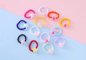 Dettaglio di 12 anelli di perline colorate elasticizzate con stelle in resina cangiante