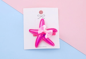 Macro shot of a purple starfish hair clip with a pink tulle bow on a display card