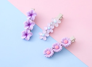 Detailsicht auf drei lila Blumen-Haarspangen aus Kunstharz auf einem rosa Hintergrund