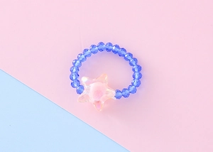 Dettaglio dell'anello con perline e stella in acrilico su sfondo rosa e azzurro pastello