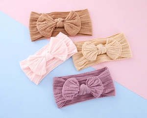 Detail of four knit baby headbands with large bows in pink, lilac, khaki, and beige colors