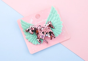 Détail d'une barrette Pegasus à paillettes roses avec ailes vertes sur carte rose