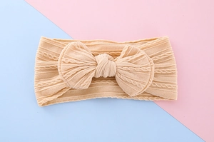 Close-up of beige knitted baby headband featuring a large bow and cable knit texture