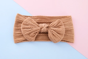 Macro detail of caramel knitted baby headband featuring ribbed texture and large bow