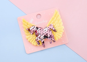 Détail d'une barrette Pegasus à paillettes roses avec des ailes jaunes sur carte