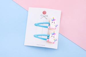Dettaglio di due fermagli per capelli a forma di unicorno glitter blu su cartoncino