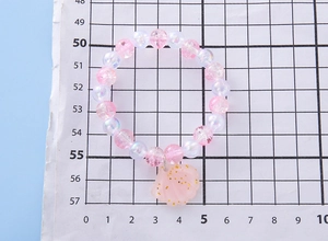 Pink beaded bracelet with shell pendant measured on scale paper for girls