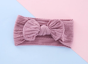 Close-up of baby knitted headband in dusty pink with a large textured bow detail
