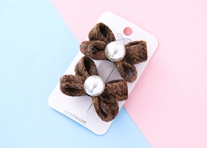 Dettaglio di fermagli per capelli a fiocco in tweed marrone con perle e carta