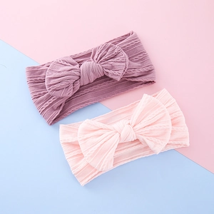 Two floral baby bow headbands in purple and pink with textured cable knit patterns