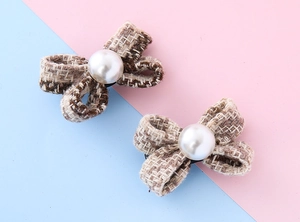 Dettaglio del fermaglio a fiocco in tweed con perla su sfondo rosa e azzurro