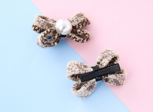 Dettaglio di fermagli per capelli a fiocco in tweed marrone con perle su sfondo blu
