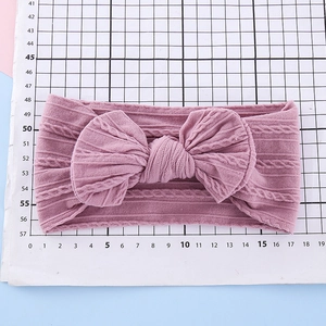 Knitted floral baby headband in dusty pink with a large bow on a measurement grid