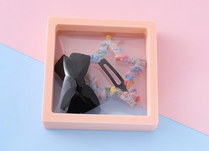 Détail du coffret cadeau rose avec une pince à nœud noir et épingle à cheveux étoile multicolore