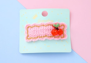 Détail d'une barrette en tricot rose avec cerises rouges et chaîne dorée élégante