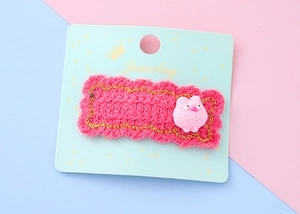 Détail d'une pince à cheveux en tricot rose avec bordure dorée et motif animal