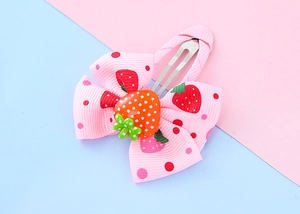 Close-up of pink ribbon hair clip with strawberry pattern and resin charm detail