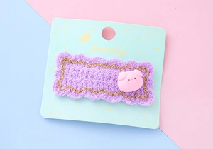 Détail de la pince à cheveux tricotée violette avec breloque cochon rose sur carte de luxe