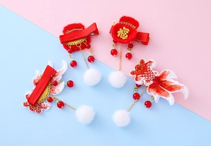 Detail view of New Year fish hair clips with embroidery, red tassels and faux fur balls