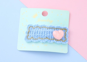 Vue détaillée d'une pince à cheveux en tricot bleu avec cœur rose sur carte de support