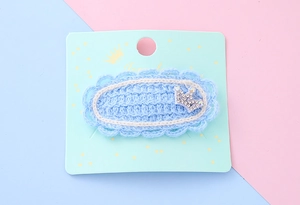 Détail d'une pince à cheveux tricotée bleu clair avec dentelle et couronne de strass