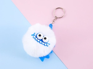 Detail shot of a white fluffy monster keychain with blue eyes and a funny smile
