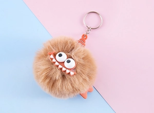 Close-up of a funny monster plush keychain with big eyes and orange hat on pink background
