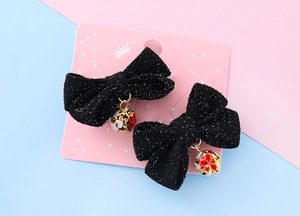 Close-up of black glitter hair bows with colorful bell pendants on pink card