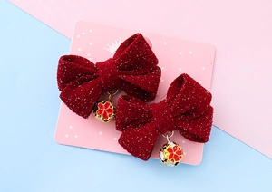 Close-up of red velvet bow hair clips with golden floral bells on a display card