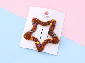 Vue détaillée d'une pince à cheveux en laine marron en forme d'étoile avec pompons colorés