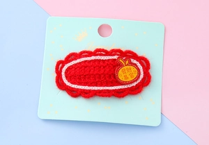 Nahaufnahme der roten gestrickten Haarspange mit Apfelstickerei und Glückssymbolen