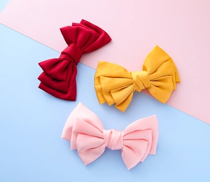 Three large satin bow hair clips in red, yellow, and pink with a soft silk texture
