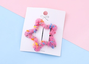 Détail d'une pince à cheveux étoile en tricot rose avec des points colorés sur carte