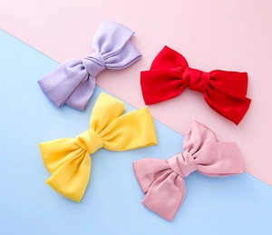 Macro detail of four satin bow hair clips in purple, red, yellow and pink on pastel background