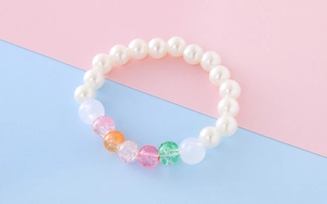 Detailed close-up of girls beaded bracelet with white pearls and colorful crackle beads