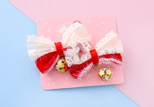 Detailed pair of red bow hair clips with white lace trim and gold bells on display card