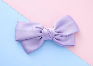 Detail of light purple fabric bow hair clip featuring satin texture on pastel background