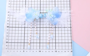 Detail showing blue flower hair clips with white feathers and pearl tassels on a grid mat